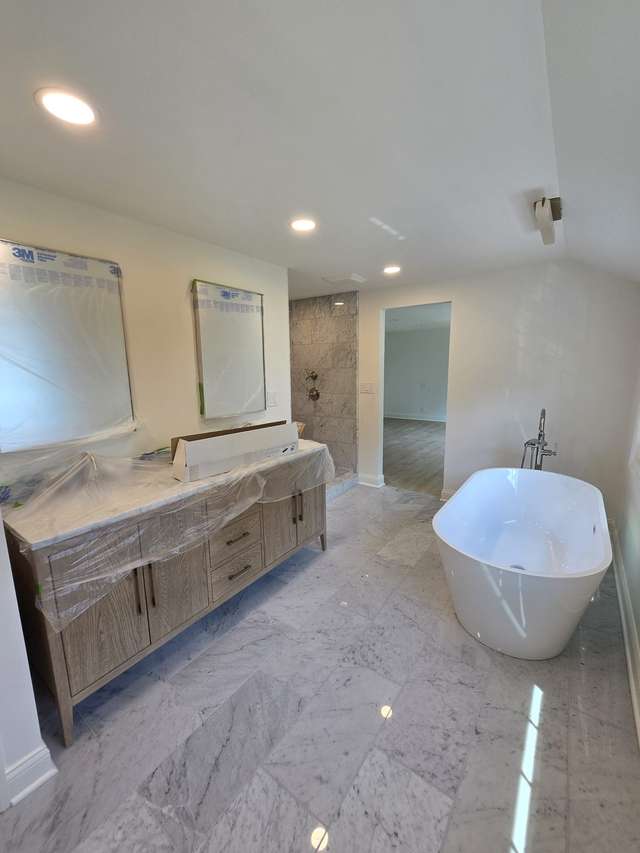 Bathroom remodel in progress with a freestanding tub, long vanity, and polished marble-look floor tile.