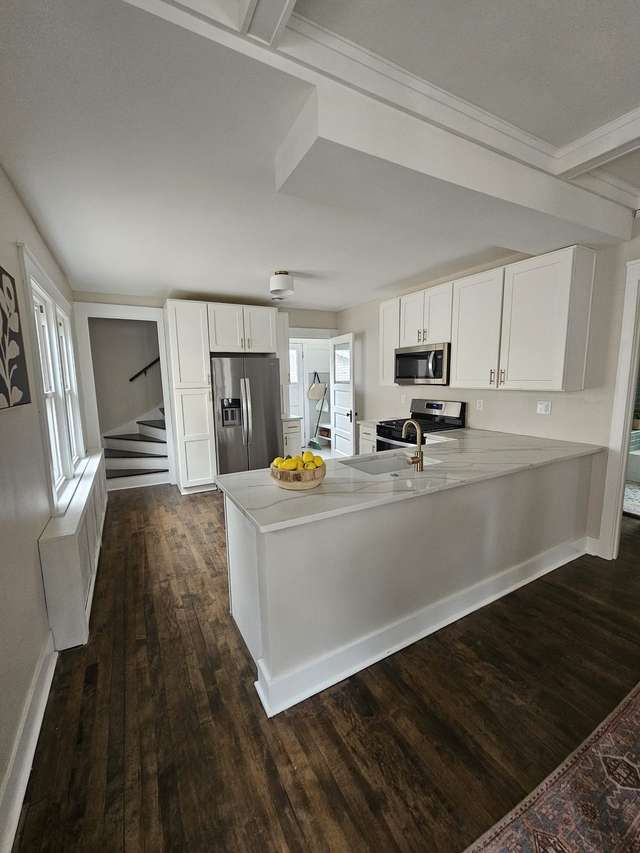 Bright white kitchen with a large island, stainless steel appliances, and dark wood flooring.
