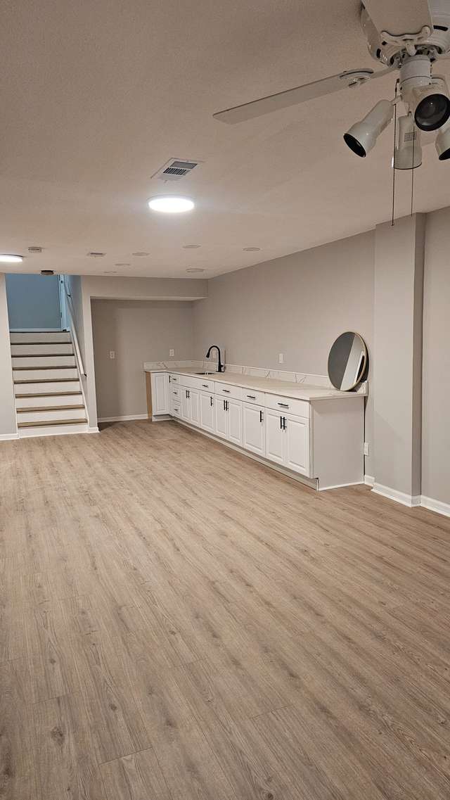 Finished lower-level room with white built-in cabinets, a sink, and open floor space.