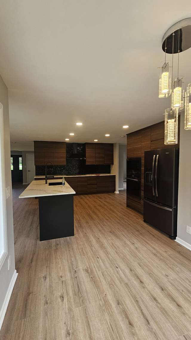 Modern dark wood kitchen with a large island, pendant lighting, and wood-look flooring.