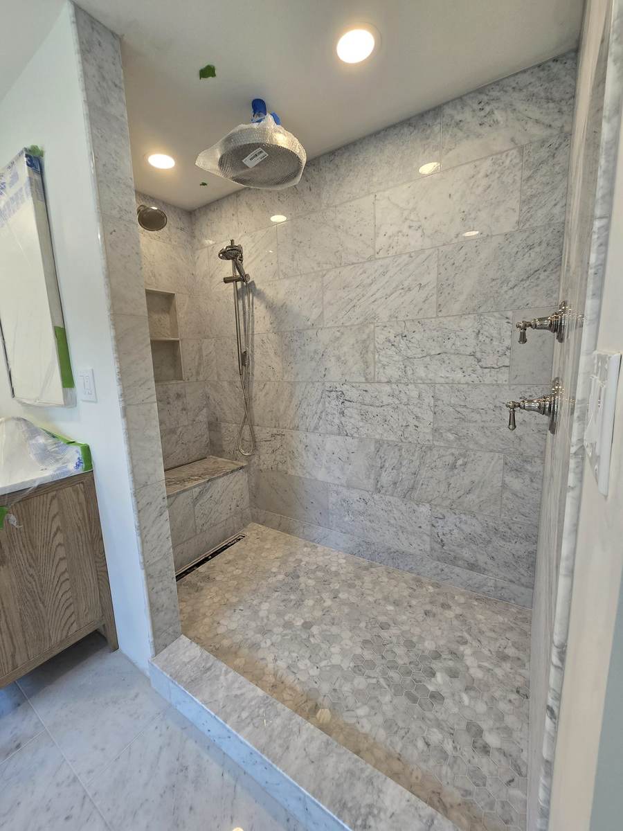 Marble-look walk-in shower with built-in bench, handheld shower, wall controls, and mosaic tile floor.