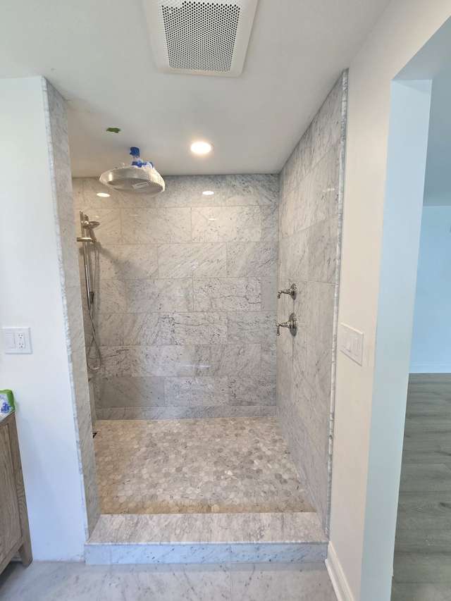 Walk-in shower with large-format marble-look wall tile during final installation work.