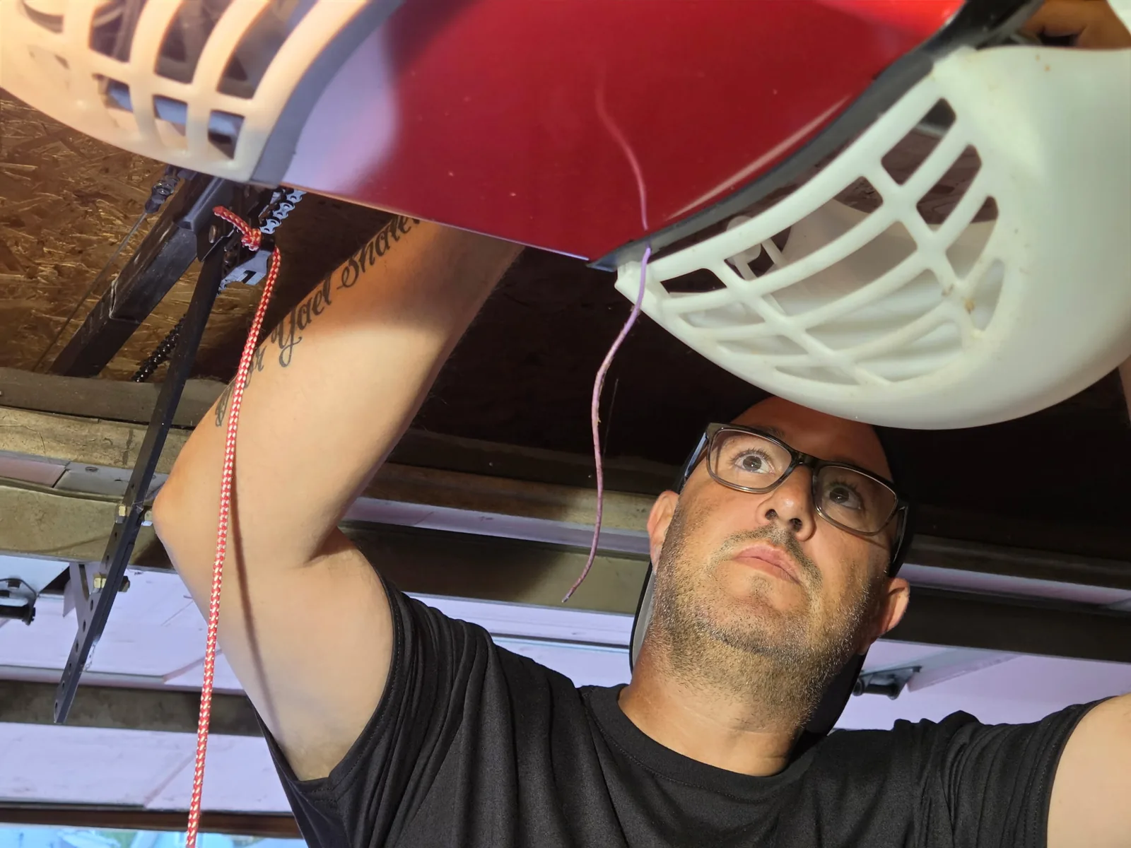 Technician reaching up to adjust a garage door opener unit.