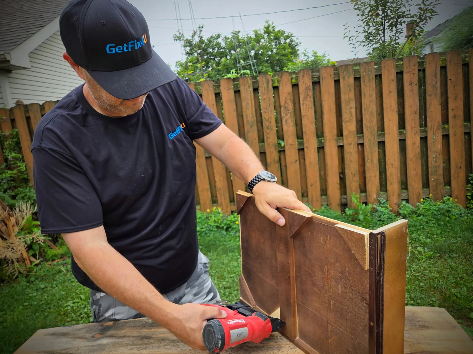 Technician assembling a flat-pack furniture drawer unit outdoors with a cordless driver.