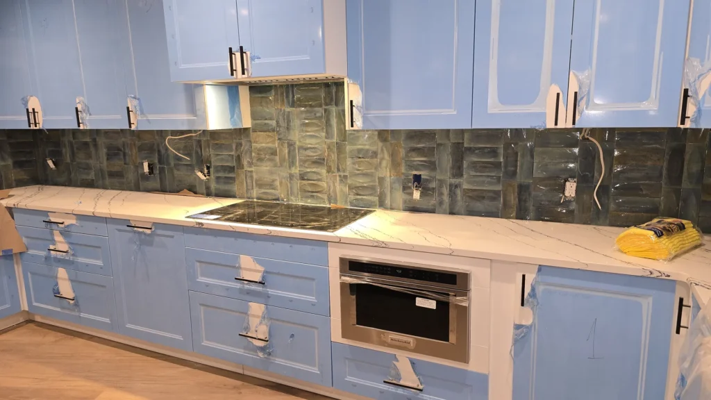 Near-finished kitchen with painted cabinets, marble-look countertops, tile backsplash, and range hood installed.