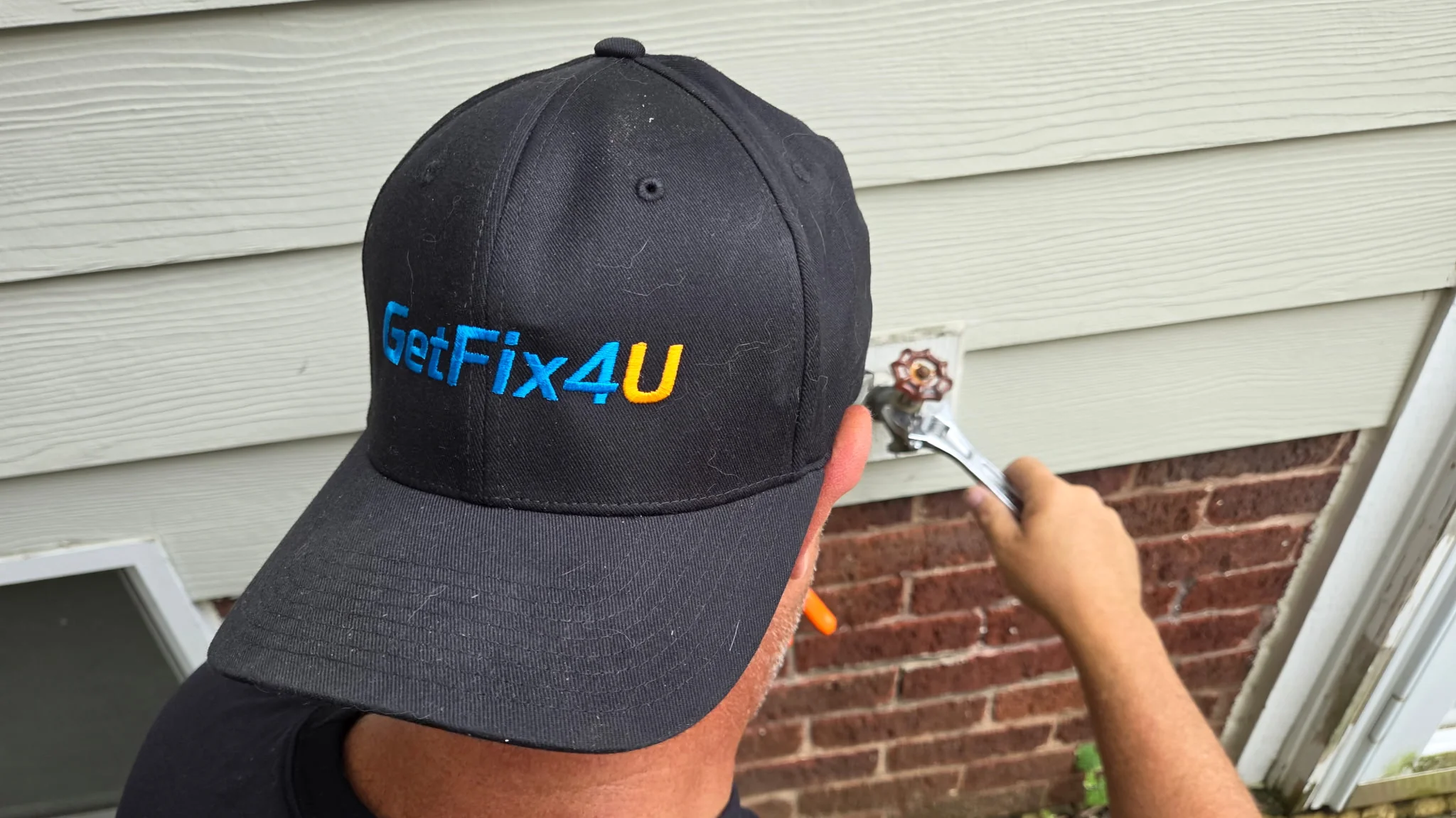 Technician using a wrench to repair an outdoor spigot on a home's exterior.