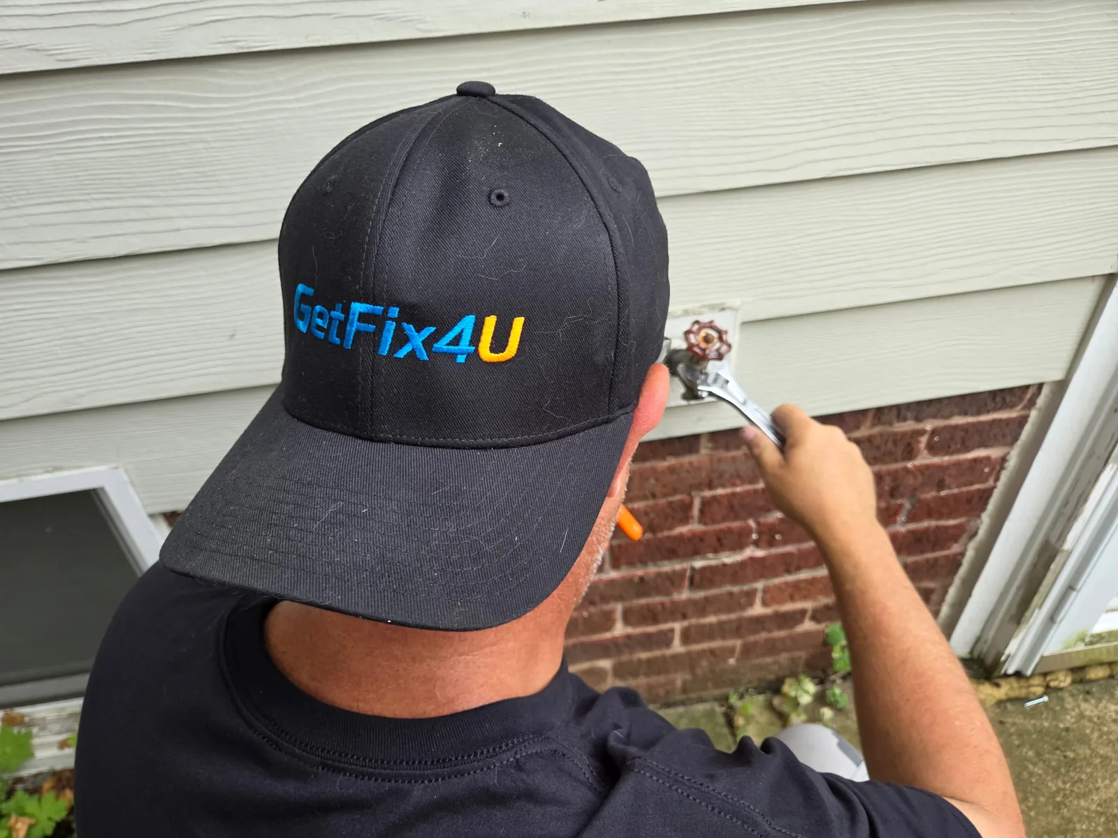 Technician using a wrench to repair an outdoor spigot on a home's exterior.